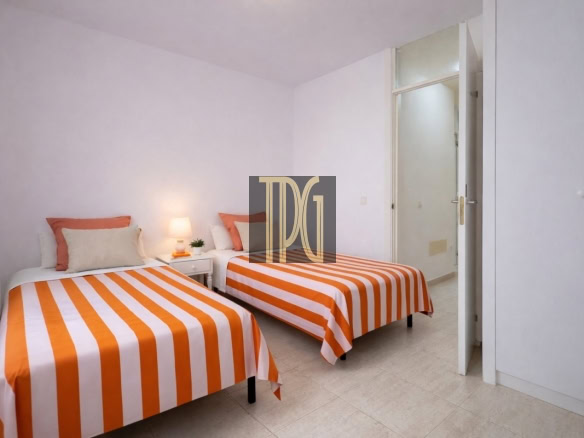 Twin bedroom with two single beds, orange-and-white striped duvets, white pillows, a small bedside table with a lamp and plant, and a closet nearby.