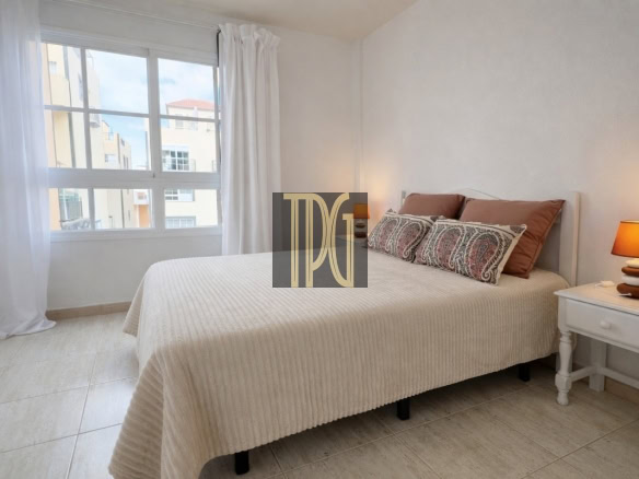 Bright bedroom with a white bedspread, decorative pillows, a white nightstand, and an orange-lamped lamp near the bed.