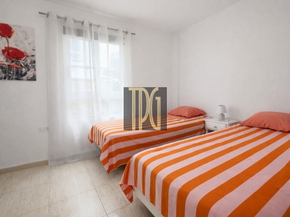 Twin bedroom with two single beds in orange-and-white striped linens, a white nightstand between them, lamp, and a large window with sheer curtains