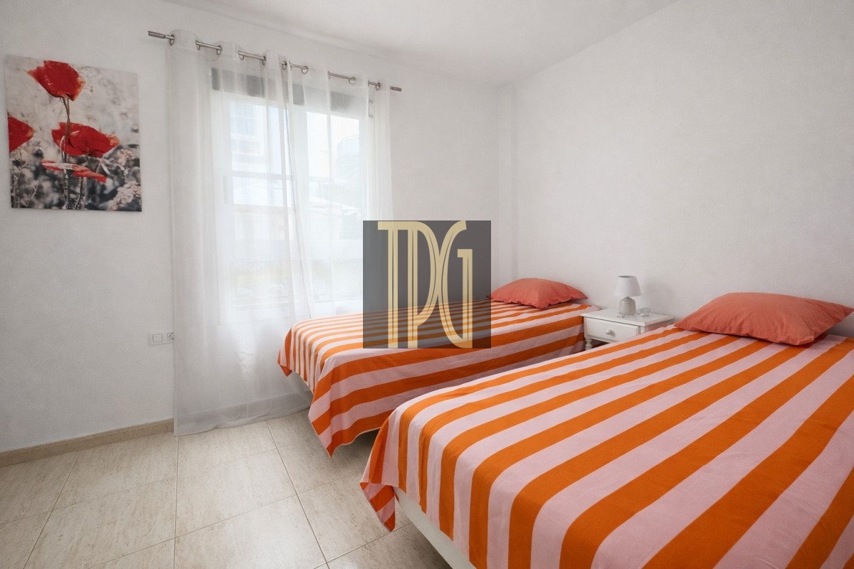 Twin bedroom with two single beds in orange-and-white striped linens, a white nightstand between them, lamp, and a large window with sheer curtains