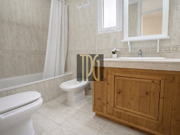 Bathroom with tub and shower curtain, toilet, bidet, and wooden vanity with sink and mirror.