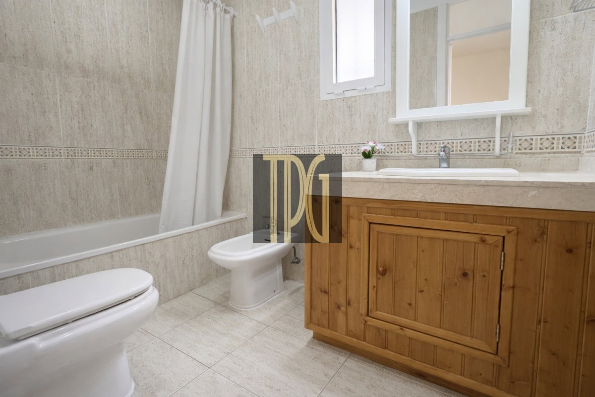 Bathroom with tub and shower curtain, toilet, bidet, and wooden vanity with sink and mirror.