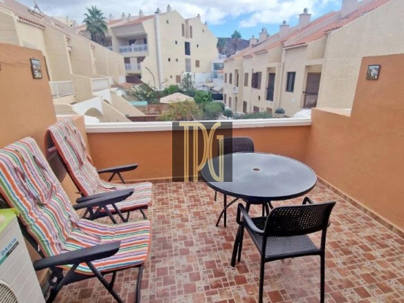 Balcony terrace with orange walls, striped lounge chairs, a round glass table and black chairs, with buildings in the background on a sunny day.