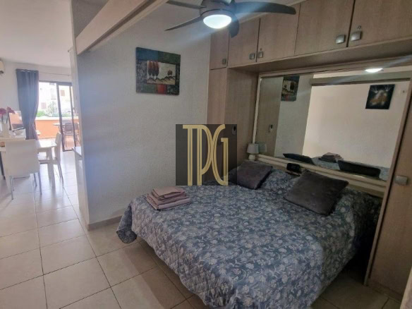 Bedroom with a blue floral bedspread, large mirrored wardrobe, and a ceiling fan; a dining area and balcony visible to the left.