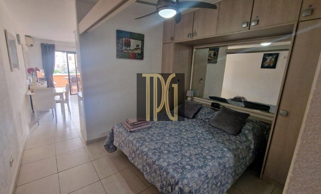 Bedroom with a blue floral bedspread, large mirrored wardrobe, and a ceiling fan; a dining area and balcony visible to the left.