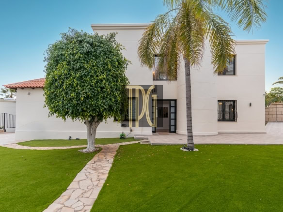 Modern beige two-story home with palm trees and a stone path leading to the front door in a landscaped yard.