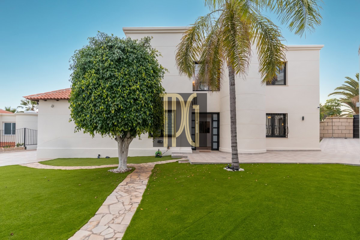 Modern beige two-story home with palm trees and a stone path leading to the front door in a landscaped yard.