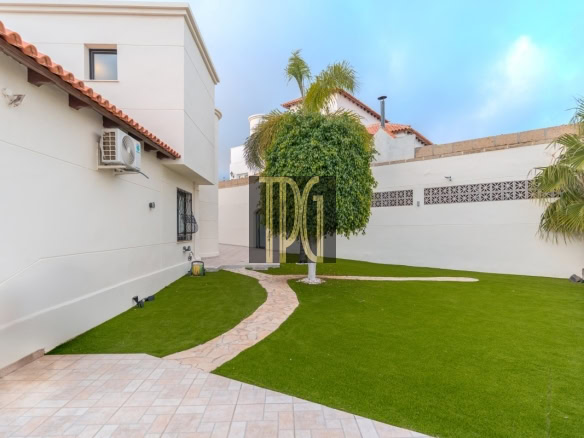 Backyard of a white house with a curved stone path, green lawn, and palm trees in the yard.