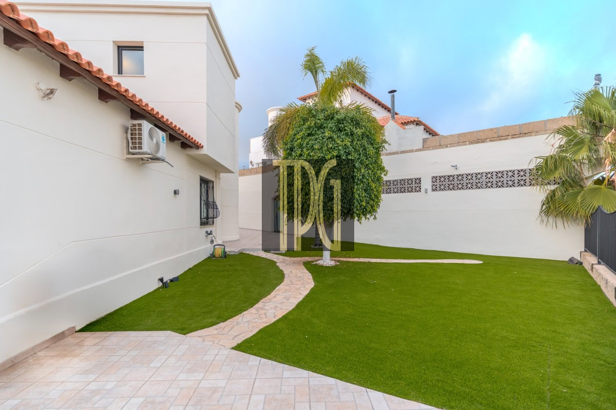 Backyard of a white house with a curved stone path, green lawn, and palm trees in the yard.