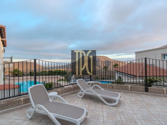 Terrace with two white lounge chairs overlooking a pool and mountain landscape in the distance, under a blue sky.