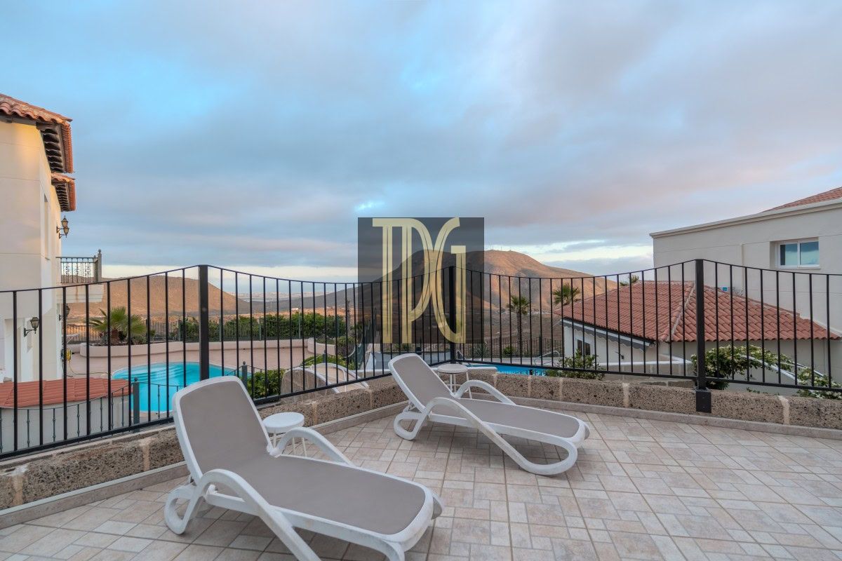 Terrace with two white lounge chairs overlooking a pool and mountain landscape in the distance, under a blue sky.