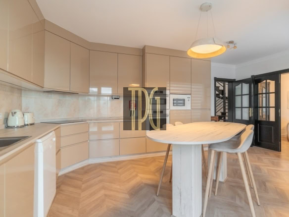 Modern beige kitchen with glossy cabinets, built-in oven and microwave, and a wooden island with stools.