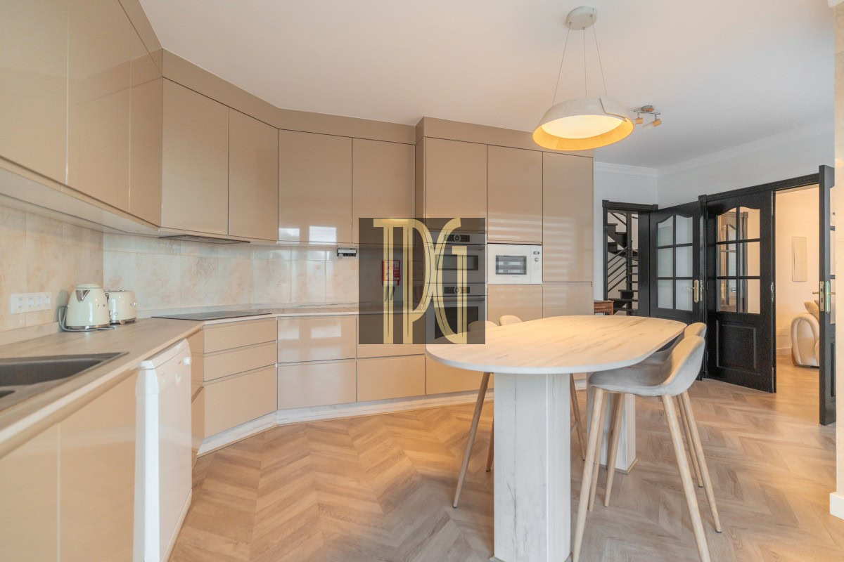 Modern beige kitchen with glossy cabinets, built-in oven and microwave, and a wooden island with stools.