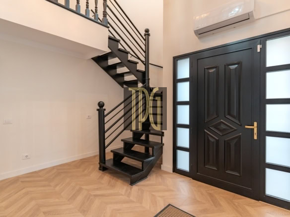 Modern foyer with a black front door featuring frosted glass panels on both sides and a black metal staircase to the left, light wood herringbone floor, and a wall-mounted AC above the door.