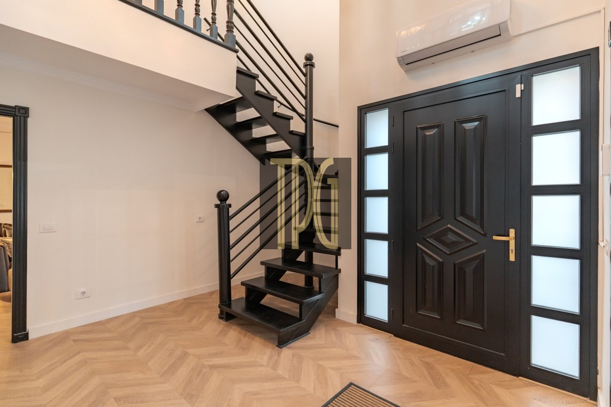 Modern foyer with a black front door featuring frosted glass panels on both sides and a black metal staircase to the left, light wood herringbone floor, and a wall-mounted AC above the door.