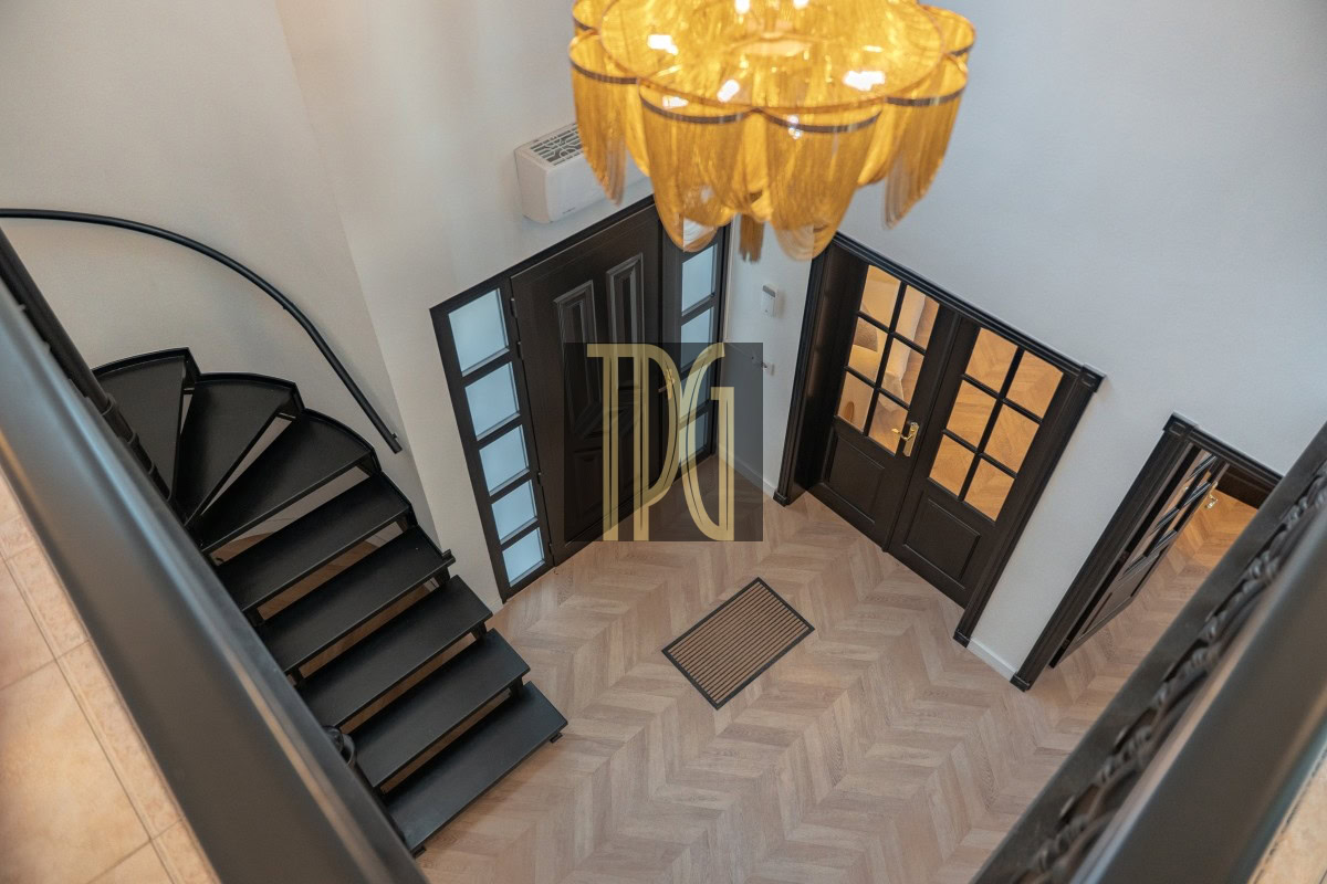 Two-story foyer with a black metal staircase on the left, dark double doors with glass panes, and a warm chandelier overhead above a herringbone floor.