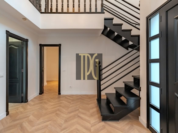 Interior entry hall with a black metal staircase, light wood herringbone floor, and dark framed doors on either side.