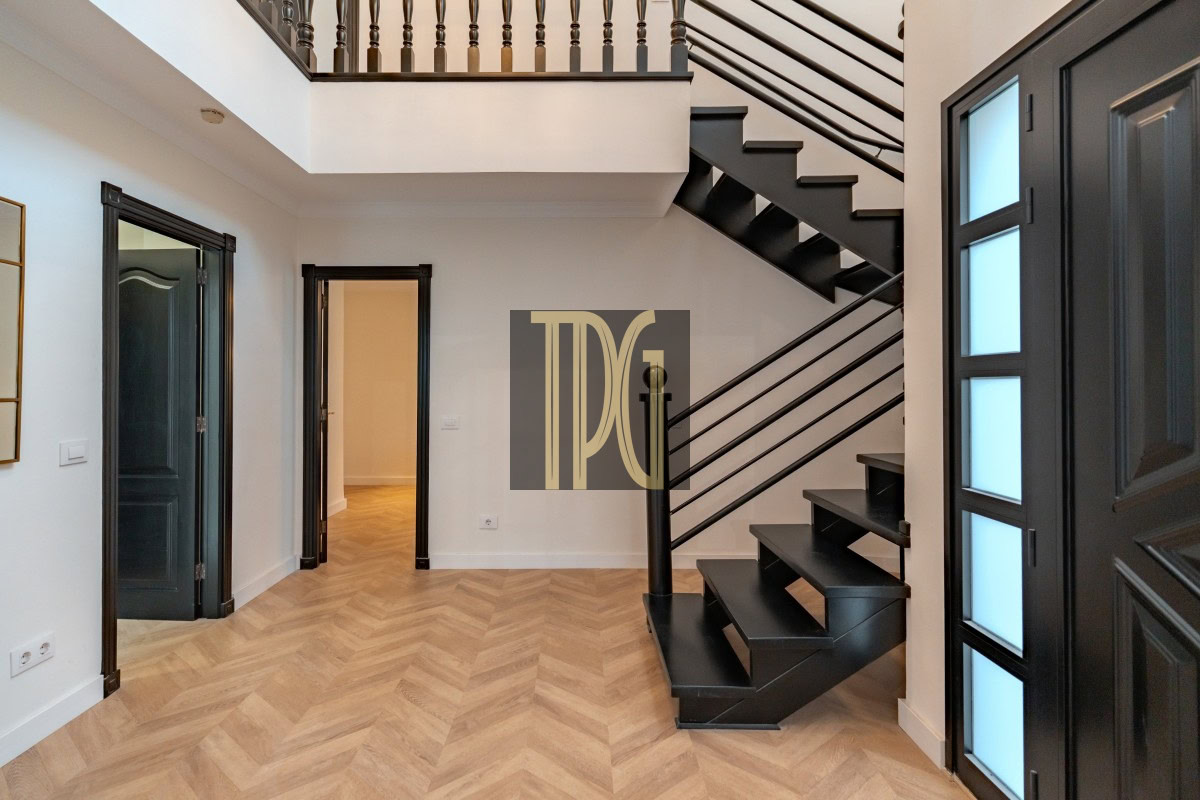 Interior entry hall with a black metal staircase, light wood herringbone floor, and dark framed doors on either side.