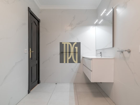 Modern bathroom with white marble walls, a wall-mounted white vanity, and a large backlit mirror above a sink.