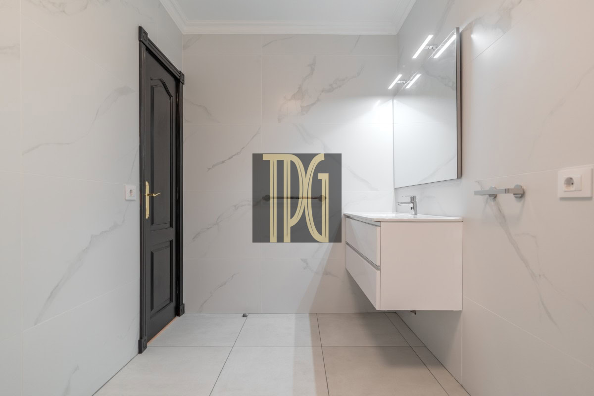 Modern bathroom with white marble walls, a wall-mounted white vanity, and a large backlit mirror above a sink.