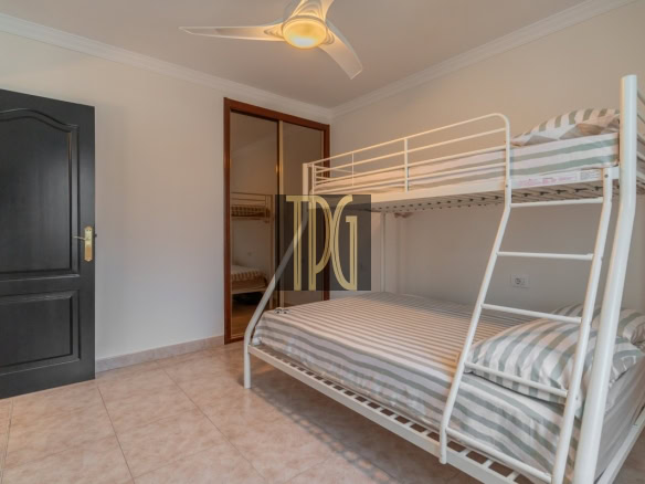 White metal bunk bed with striped gray-and-white bedding in a bright, minimal bedroom; black entry door on the left and a ceiling fan overhead.