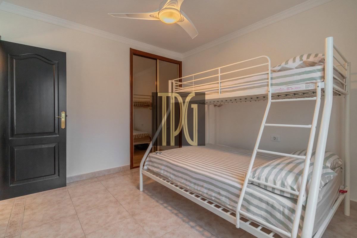White metal bunk bed with striped gray-and-white bedding in a bright, minimal bedroom; black entry door on the left and a ceiling fan overhead.