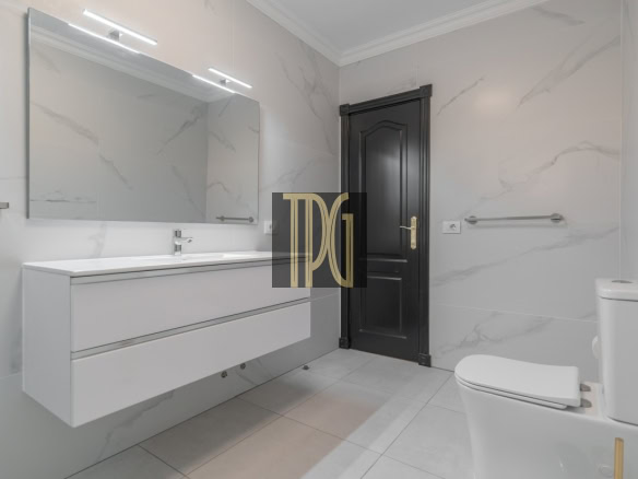 Modern white bathroom with a floating vanity, large mirror, marble walls, and a dark door.