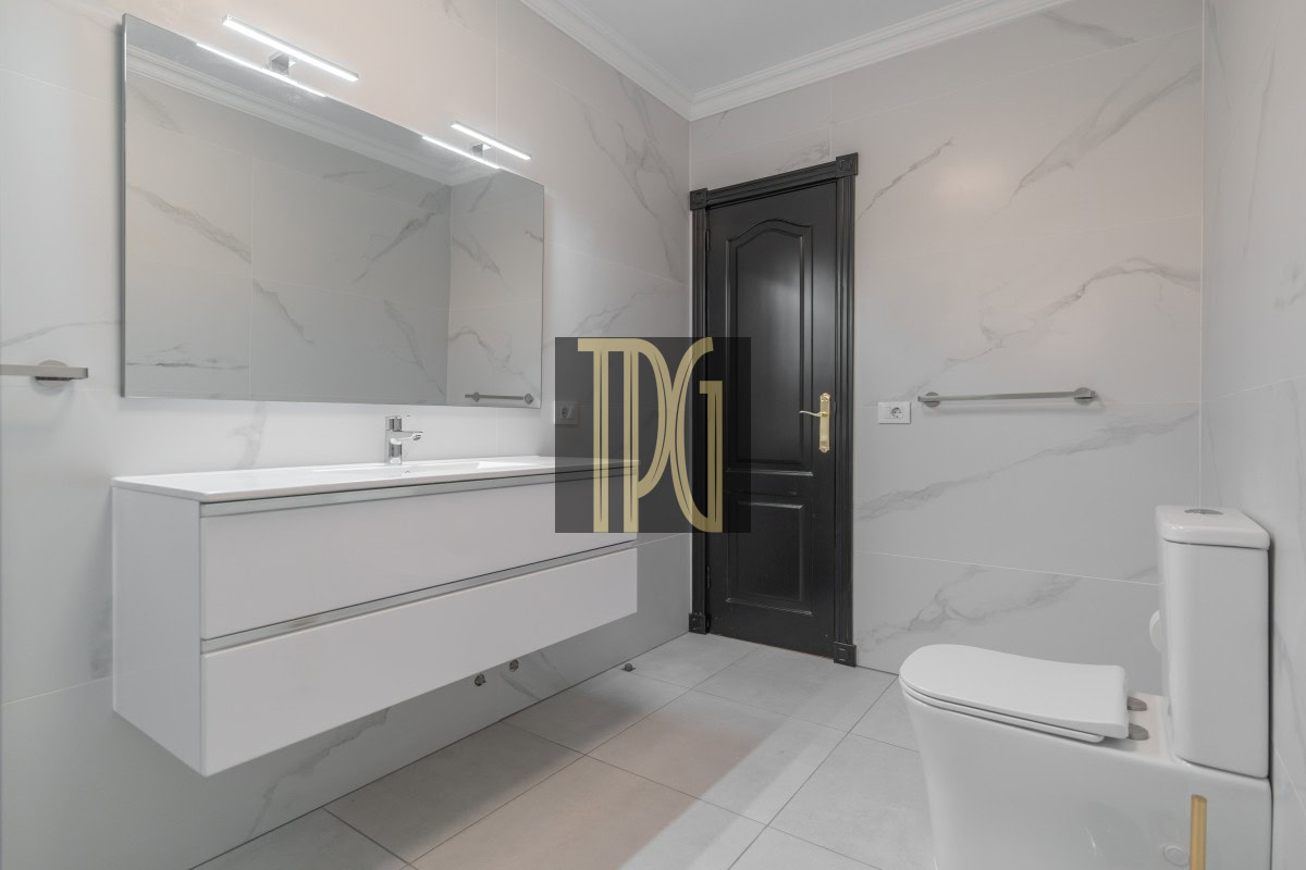 Modern white bathroom with a floating vanity, large mirror, marble walls, and a dark door.