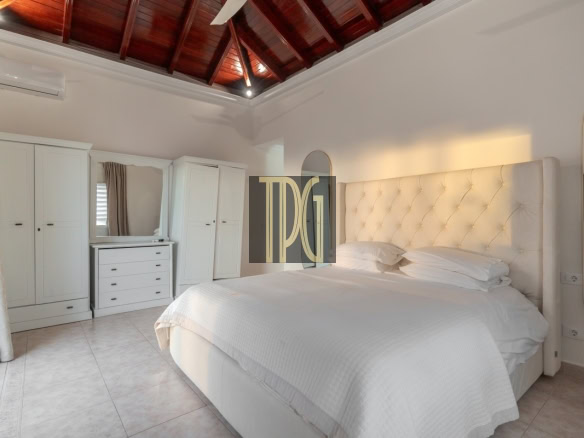 Bright, elegant bedroom with a large tufted white headboard, white bedding, and white wardrobes along the wall.