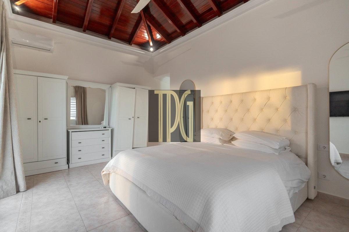 Bright, elegant bedroom with a large tufted white headboard, white bedding, and white wardrobes along the wall.