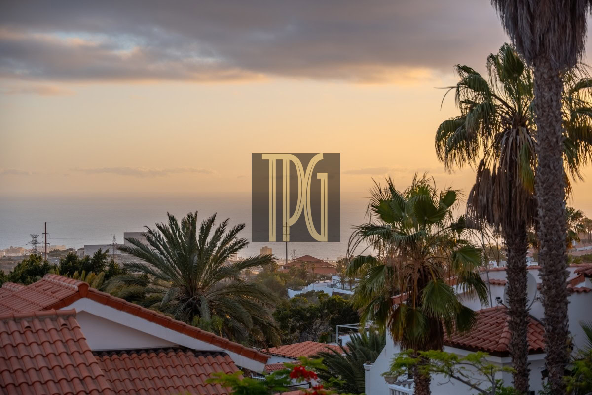 Sunset over a Mediterranean-style neighborhood with palm trees and red-tiled roofs; TDG logo centered in the scene.