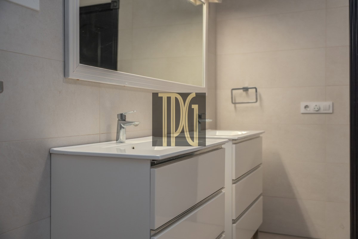 Modern bathroom vanity with two white sinks, chrome faucets, and a large wall mirror in a neutral-toned tile room.