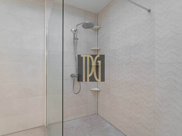 Modern walk-in shower with a glass door, a ceiling rain showerhead and handheld wand, Beige tiled walls with corner shelves.