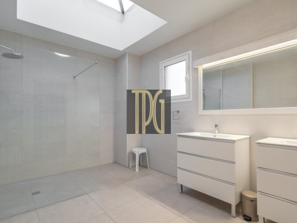 Bright, modern bathroom with a glass-walled walk-in shower, skylight, and dual white vanities.