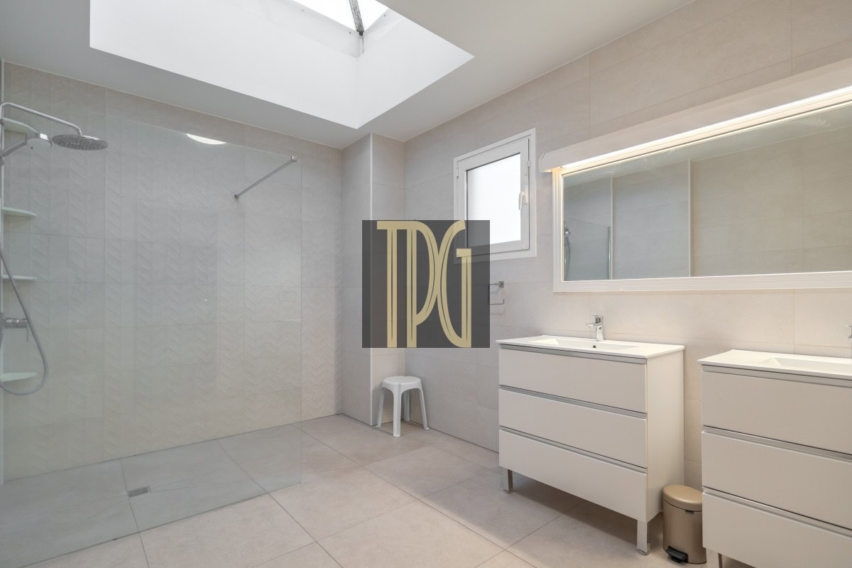 Bright, modern bathroom with a glass-walled walk-in shower, skylight, and dual white vanities.