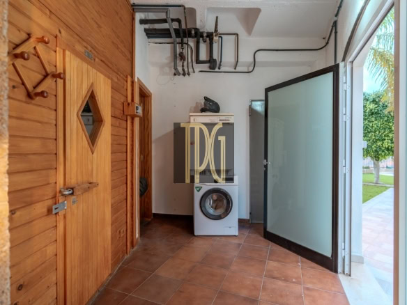 Utility laundry room with a front-loading washing machine, wooden cabinets, and an open frosted glass door to the outside yard