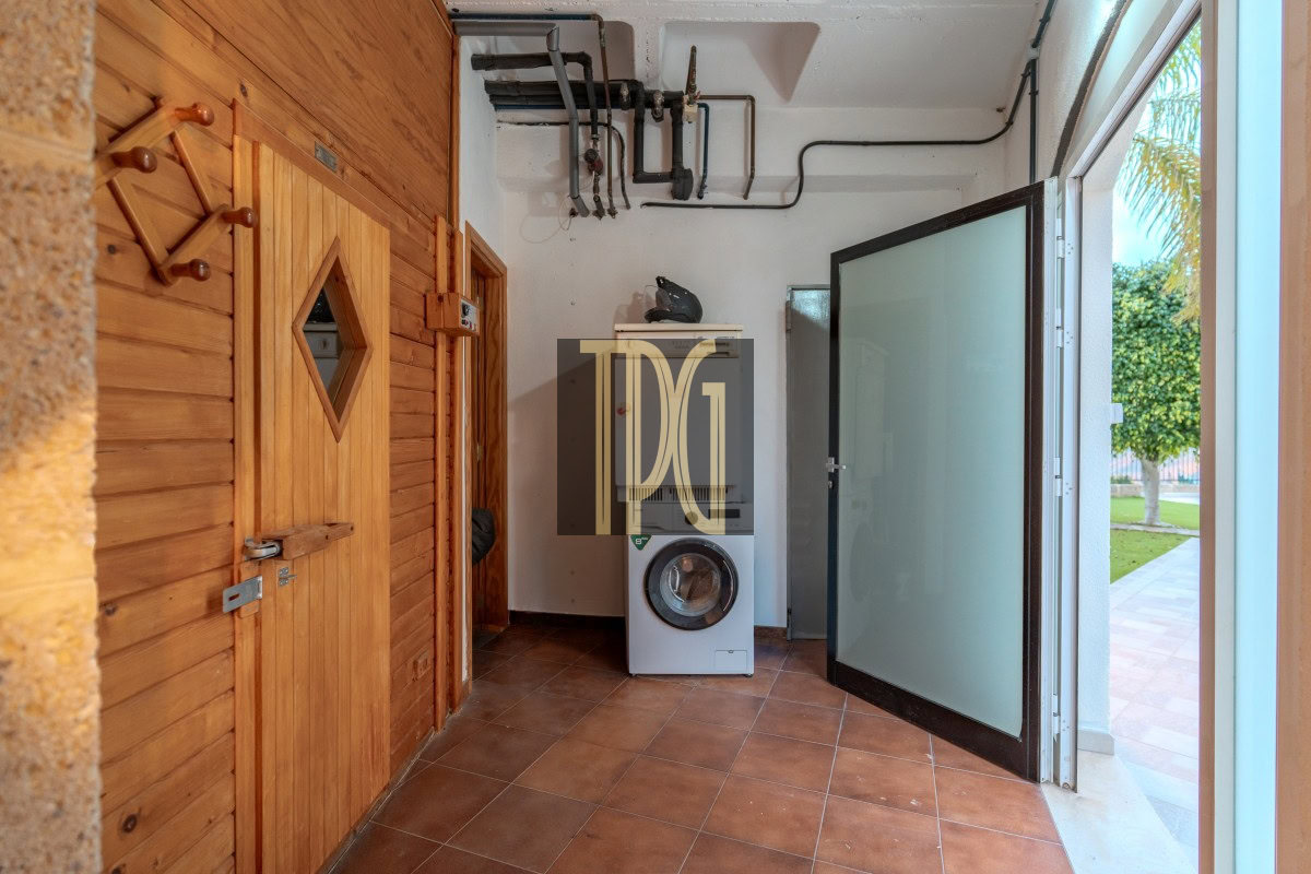Utility laundry room with a front-loading washing machine, wooden cabinets, and an open frosted glass door to the outside yard