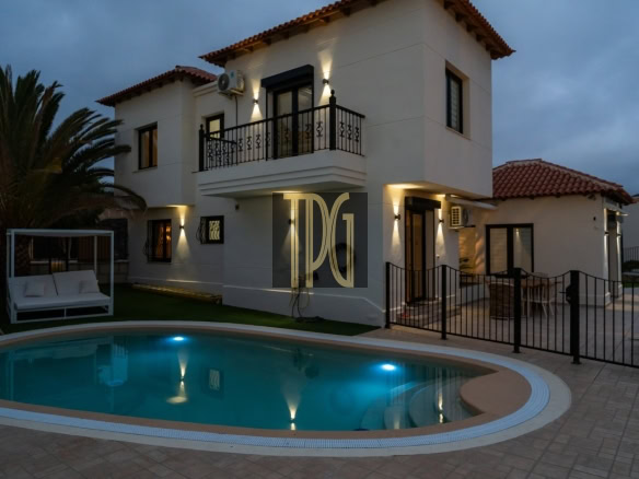 Two-story white villa with a gated patio and illuminated circular pool at dusk.