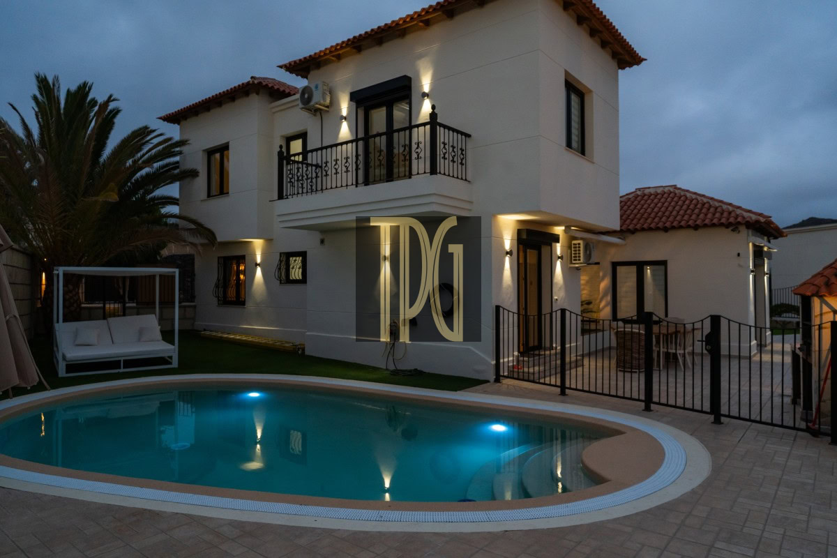 Two-story white villa with a gated patio and illuminated circular pool at dusk.