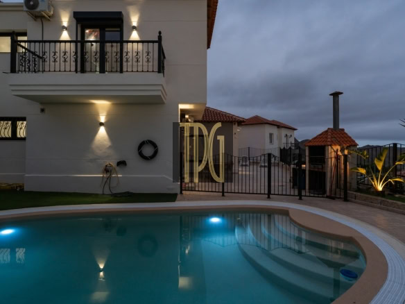 Modern white villa with a curved pool in the foreground, pool lights glowing at dusk.