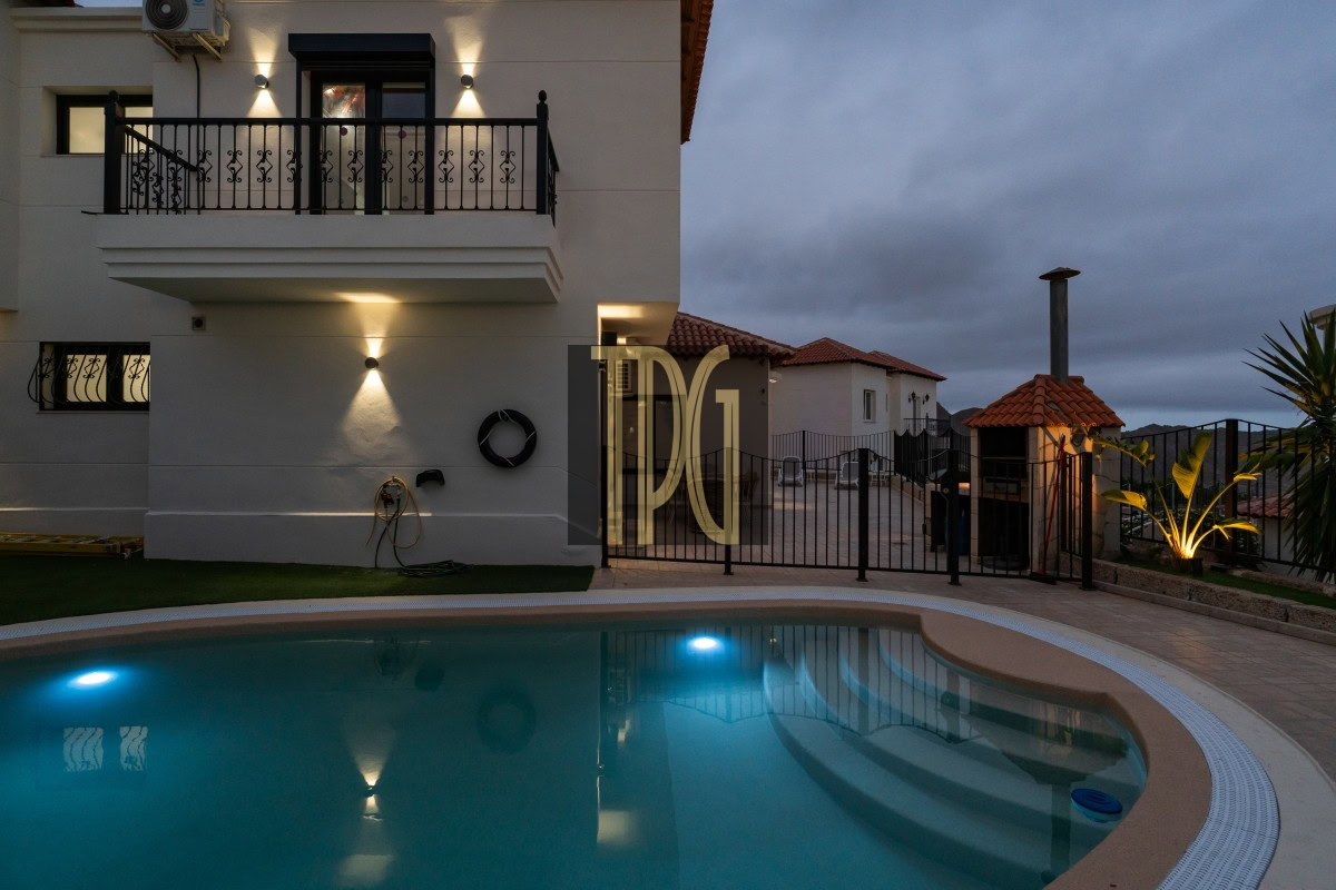 Modern white villa with a curved pool in the foreground, pool lights glowing at dusk.