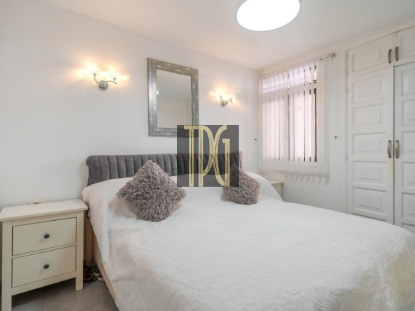 Bright bedroom with a white bedspread, grey tufted headboard, and matching cream nightstands on either side of the bed.