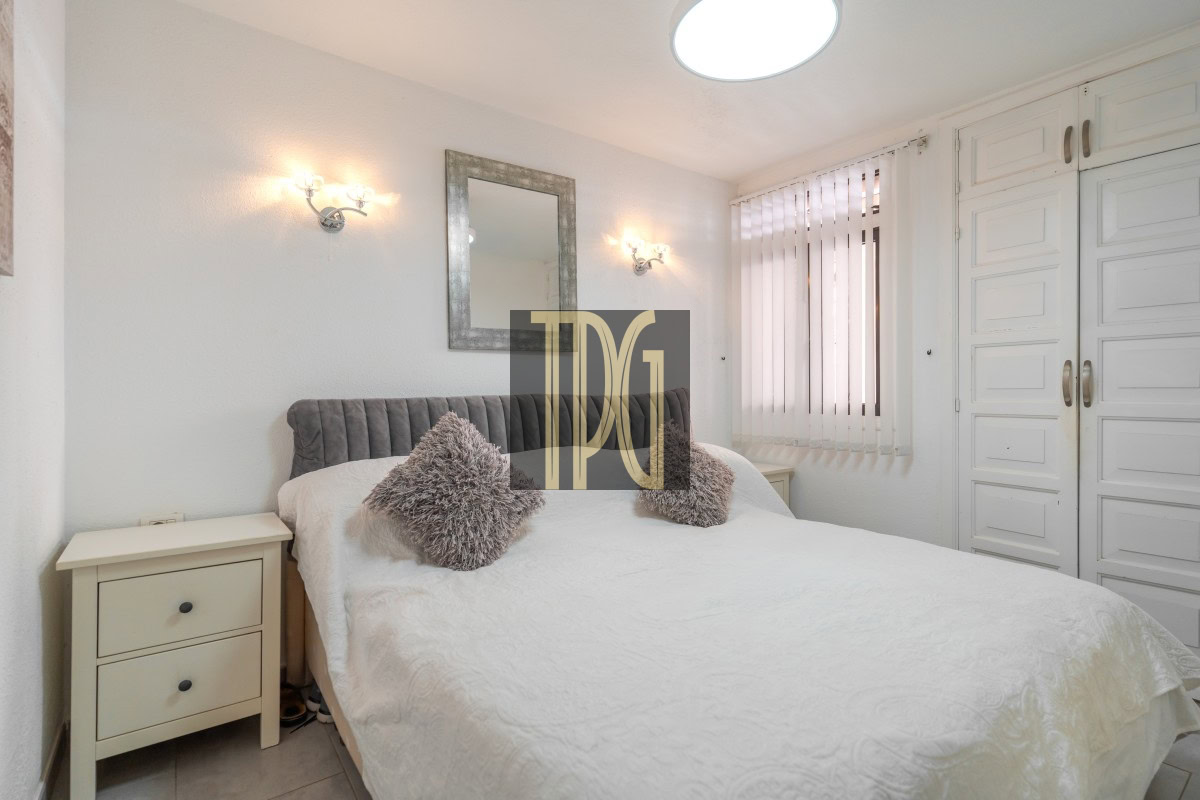 Bright bedroom with a white bedspread, grey tufted headboard, and matching cream nightstands on either side of the bed.