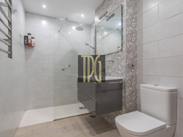 Modern bathroom with glass-enclosed shower, rainfall head, and a floating gray vanity with mirror and geometric tile accent wall on the right side.