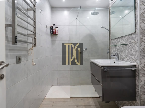 Modern bathroom with a glass-enclosed shower, wall-mounted vanity, and grey tiled walls; a towel radiator is on the left and a large mirror is above the sink.