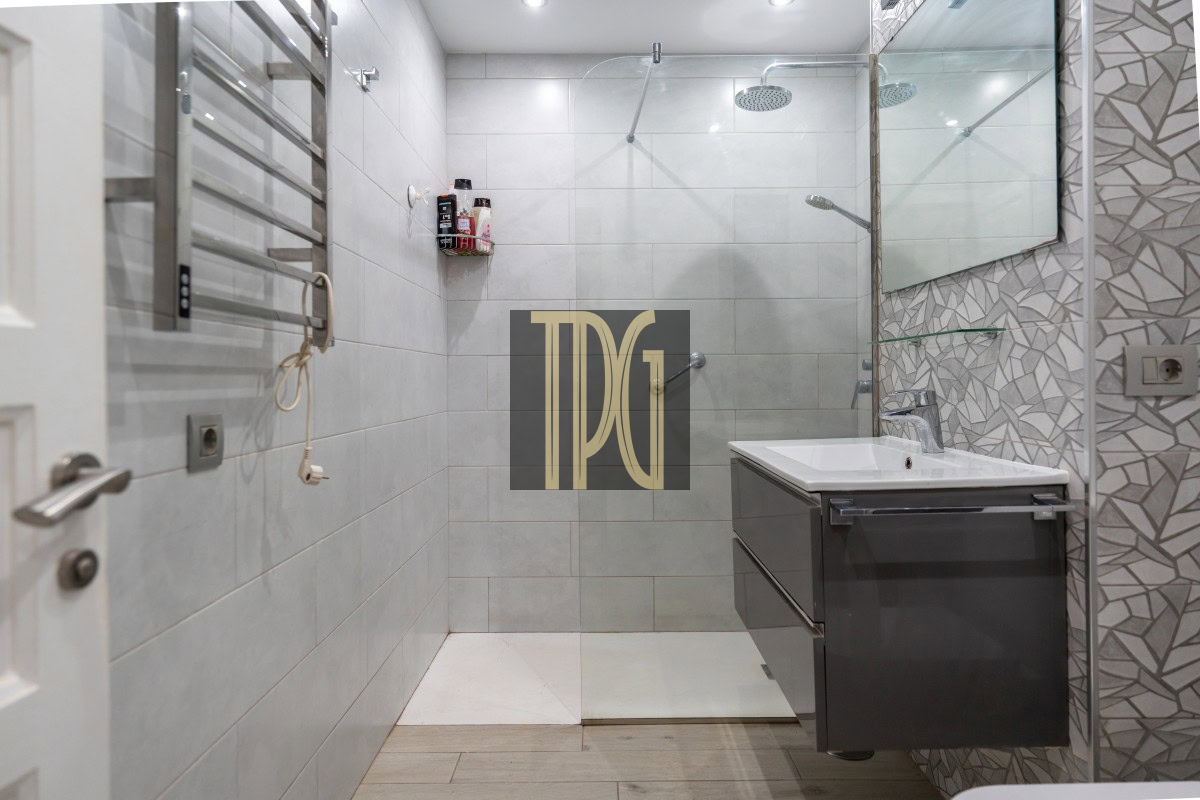 Modern bathroom with a glass-enclosed shower, wall-mounted vanity, and grey tiled walls; a towel radiator is on the left and a large mirror is above the sink.