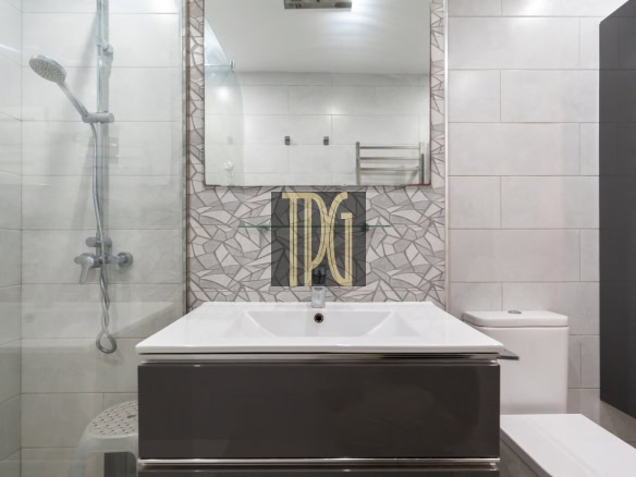 Modern bathroom with a glass shower on the left, a white sink on a dark vanity, and a geometric tiled backsplash behind the basin.