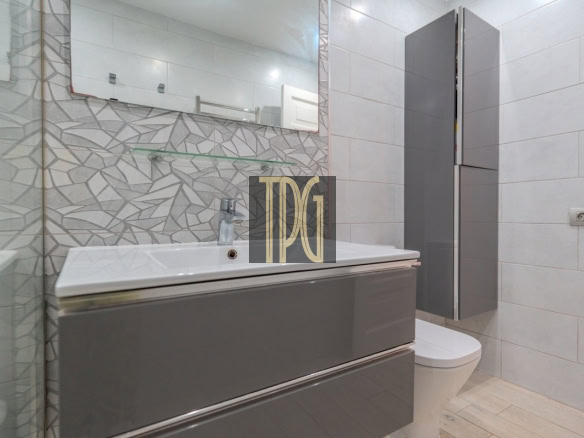 Modern bathroom with a glossy gray vanity, white sink, large mirror, geometric tiled backsplash, wall shelf, and toilet nearby.