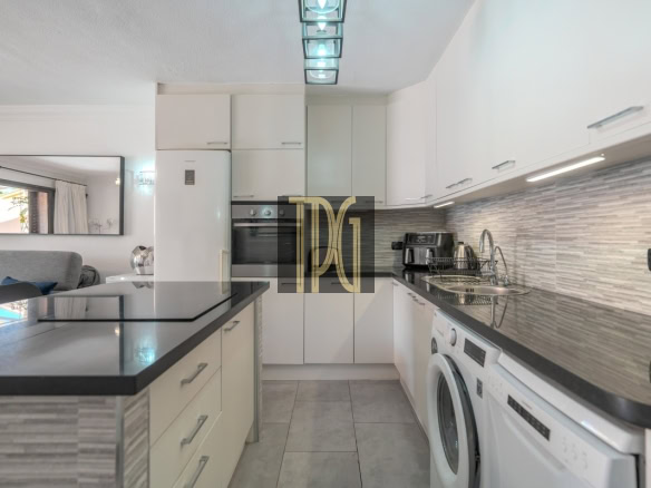 Modern white kitchen with an island, stainless steel sink, and front-loading washing machine under a gray striped backsplash.