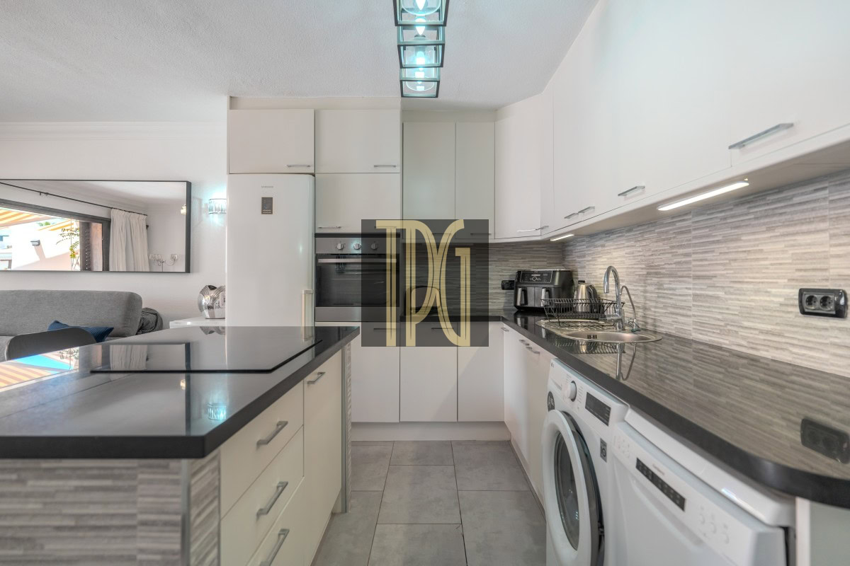 Modern white kitchen with an island, stainless steel sink, and front-loading washing machine under a gray striped backsplash.